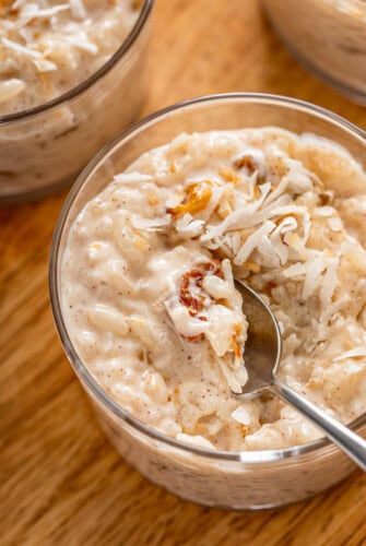 A bowl of creamy coconut rice pudding with golden raisins and topped with toasted coconut with a spoon taking a bite.