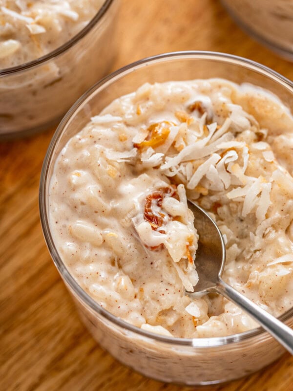 A bowl of creamy coconut rice pudding with golden raisins and topped with toasted coconut with a spoon taking a bite.