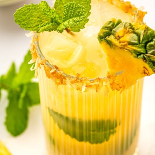 Up close image of the toasted coconut rim and fresh mint and pineapple wedge garnish on a mojito.