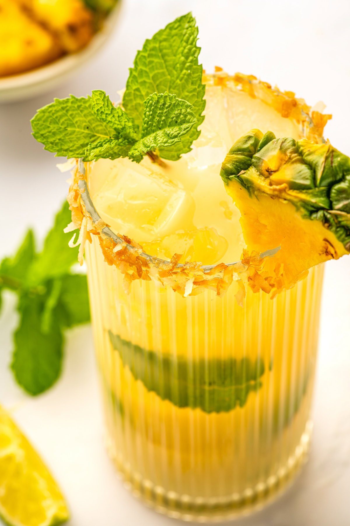 Up close image of the toasted coconut rim and fresh mint and pineapple wedge garnish on a mojito.