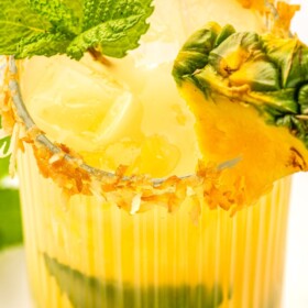 A coconut pineapple mojito served in a tall cocktail glass with a toasted coconut rim.