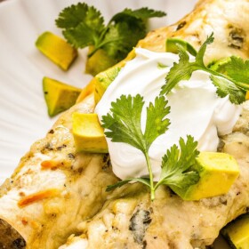 Two creamy chicken enchiladas with white sauce and avocado on a plate.