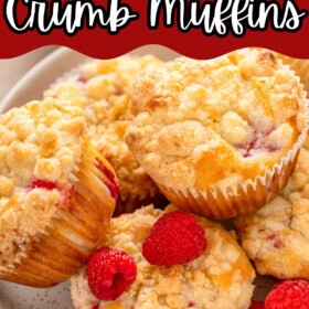 Raspberry muffins with crumb topping and white chocolate chips stacked on a plate.