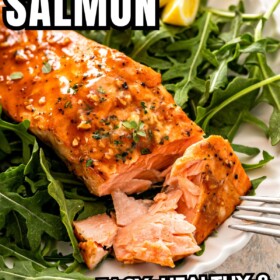 Juicy balsamic salmon over a bed of arugula on a plate with a fork cutting the flaky salmon.