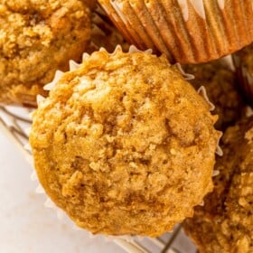 Soft and warm, brown sugar banana muffins with glistening brown sugar tops are arranged in a wire basket.