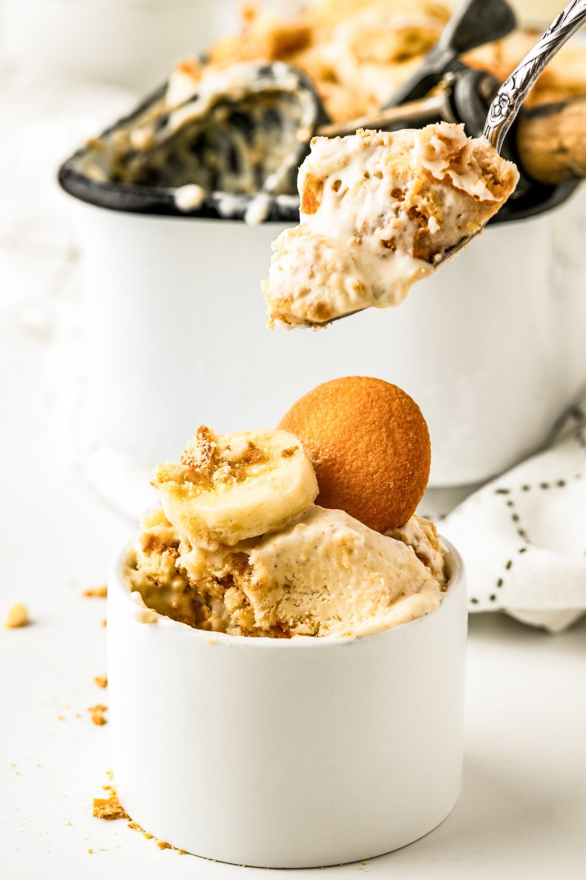 A serving of creamy banana pudding ice cream with nilla wafers and bananas in a bowl with a spoon taking a bite.