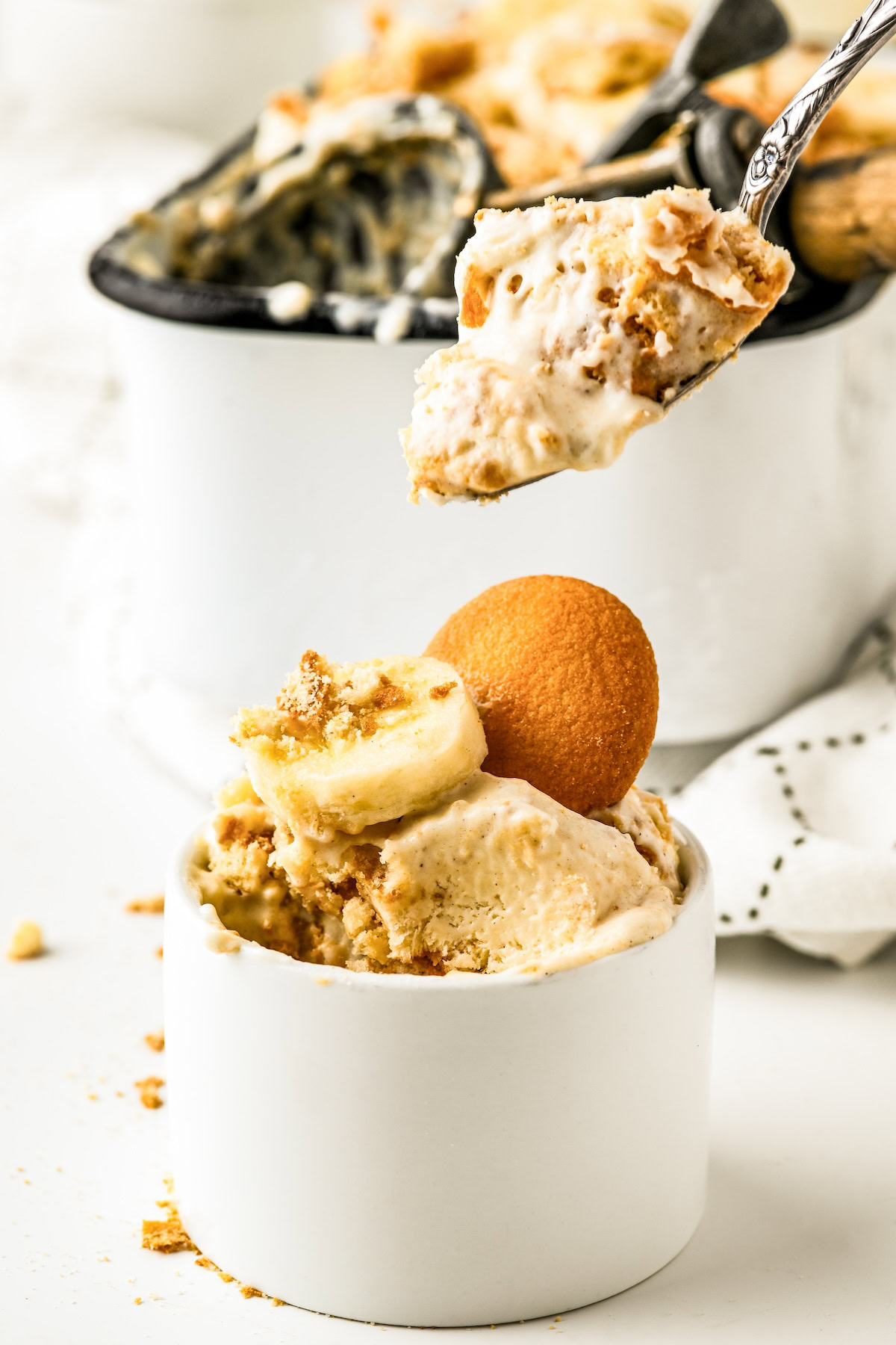 A serving of creamy banana pudding ice cream with nilla wafers and bananas in a bowl with a spoon taking a bite.