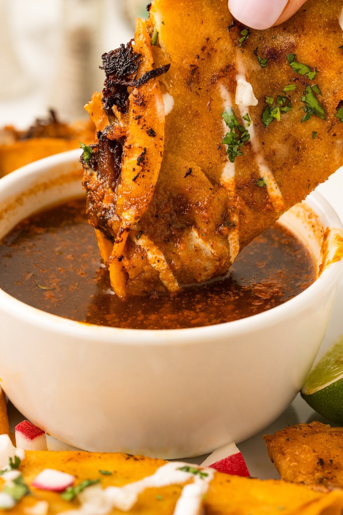 Crispy Birria Tacos being dunked in a bowl of warm birria broth.