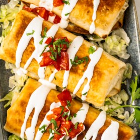 Crispy chicken chimichangas on a platter topped with sour cream, cilantro and salsa.