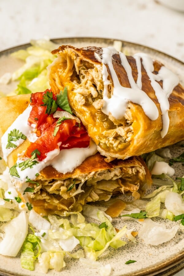 A cheesy chicken chimichanga topped with sour cream on a plate sliced in half to show to gooey filling.