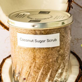 A jar of diy sugar scrub made with coconut oil sitting in a halved fresh coconut.