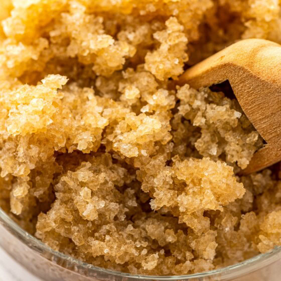 A coarse homemade sugar scrub with coconut oil in a glass jar with a wooden scoop.