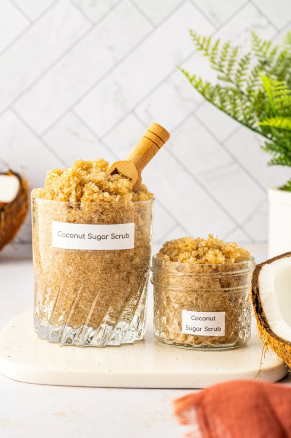 One large and one small glass jar filled with homemade sugar scrub made with coconut and vitamin e oil.