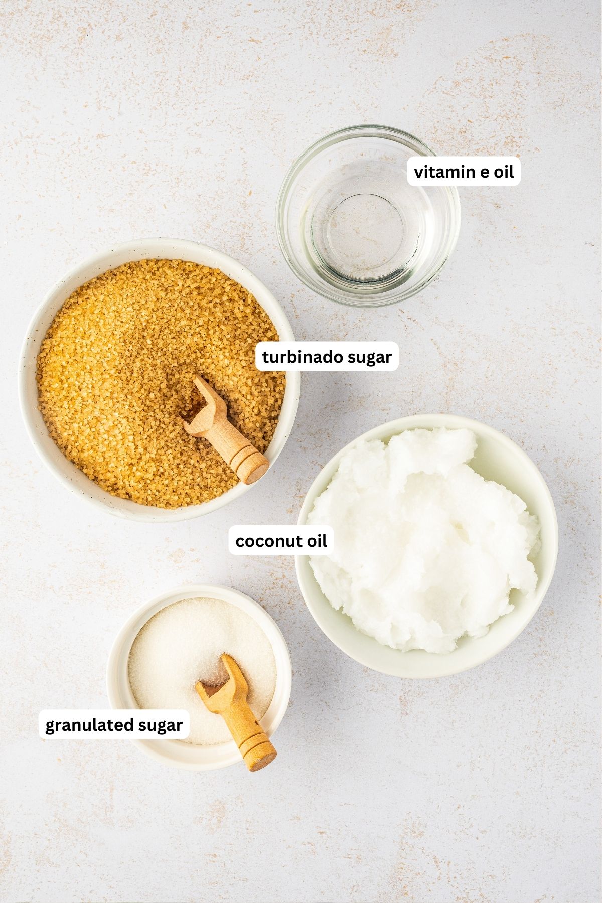 Ingredients arranged in bowls for this homemade sugar scrub recipe. From top to bottom: vitamin e oil, turbanado sugar, coconut oil and granulated sugar.