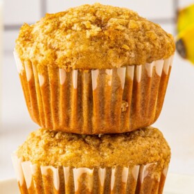 Two brown sugar banana muffins stacked on top of each other on a plate.