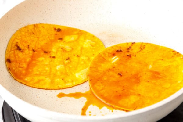 Two corn tortillas coated in birria grease in a skillet.