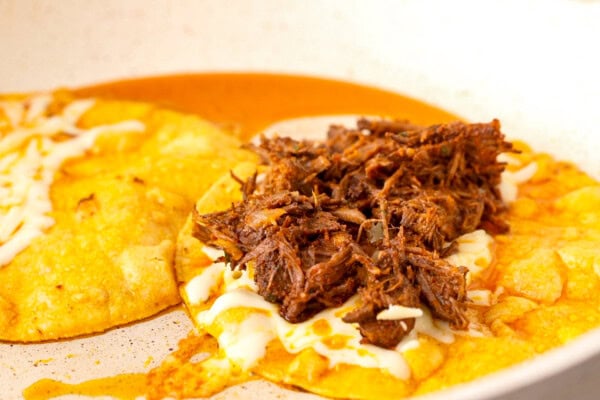 Open faced corn tortillas in a skillet stuffed with birria meat and melty cheese.