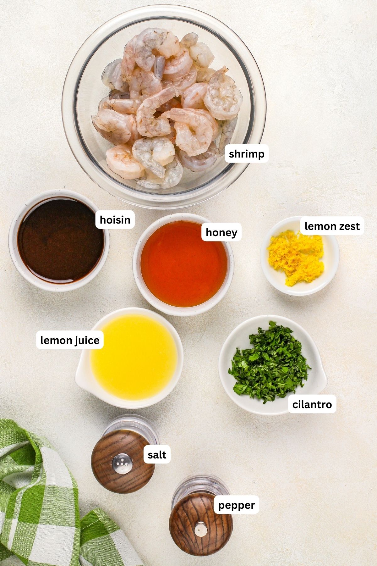 Ingredients arranged in bowls for grilled shrimp skewers recipe. From top to bottom: shrimp, hoisin sauce, honey, lemon zest, lemon juice, cilantro, salt and pepper.