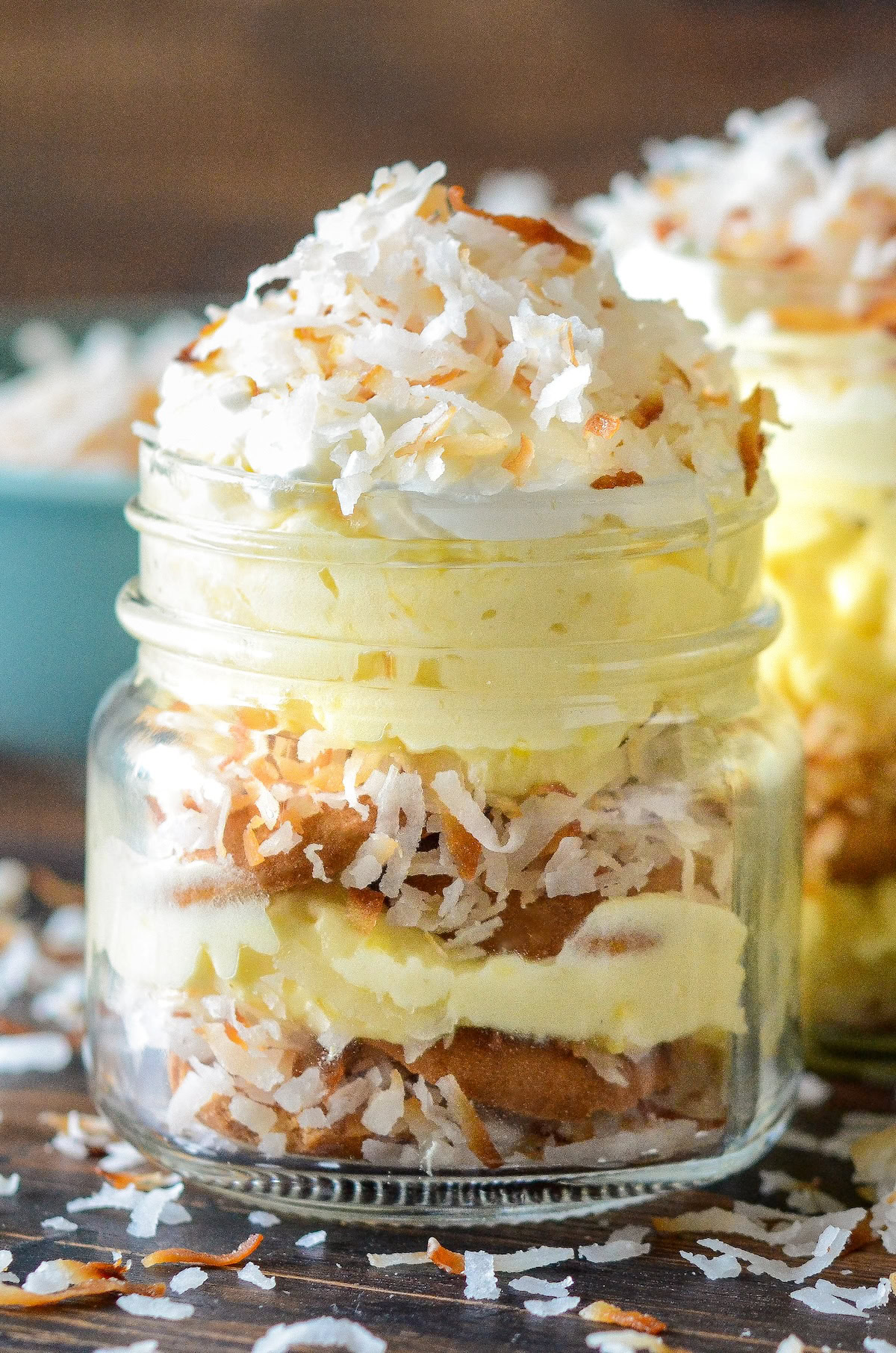 A mason jar of creamy coconut pudding with layers of vanilla wafers with whipped cream and more toasted shredded coconut on top.