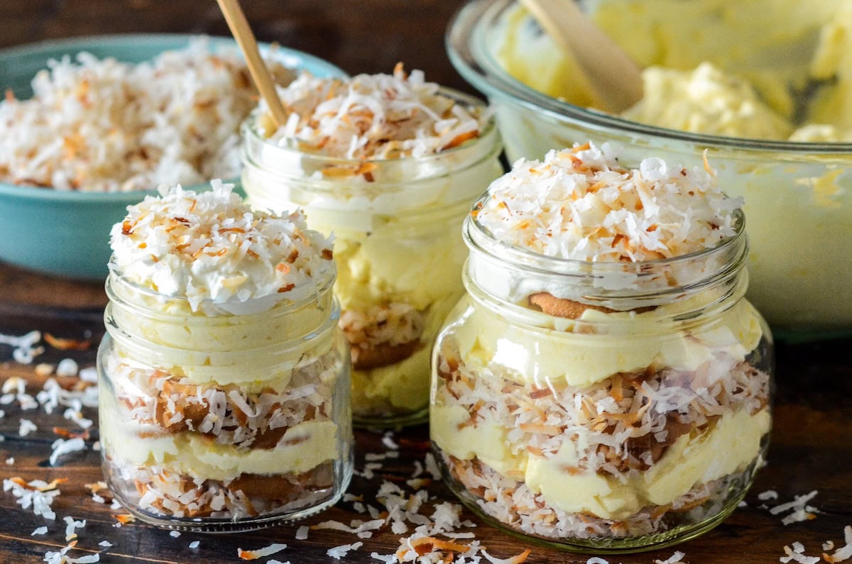 Three jars of coconut pudding with layers of toasted shredded coconut, vanilla wafers and creamy coconut pudding.
