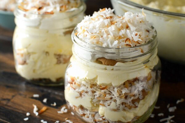 A jar of coconut pudding with layers of pudding, toasted shredded coconut and vanilla wafer cookies.