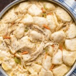 A pot filled with chicken and dumplings with fluffy biscuits and tender chicken in a creamy soup with carrots, onion and celery.