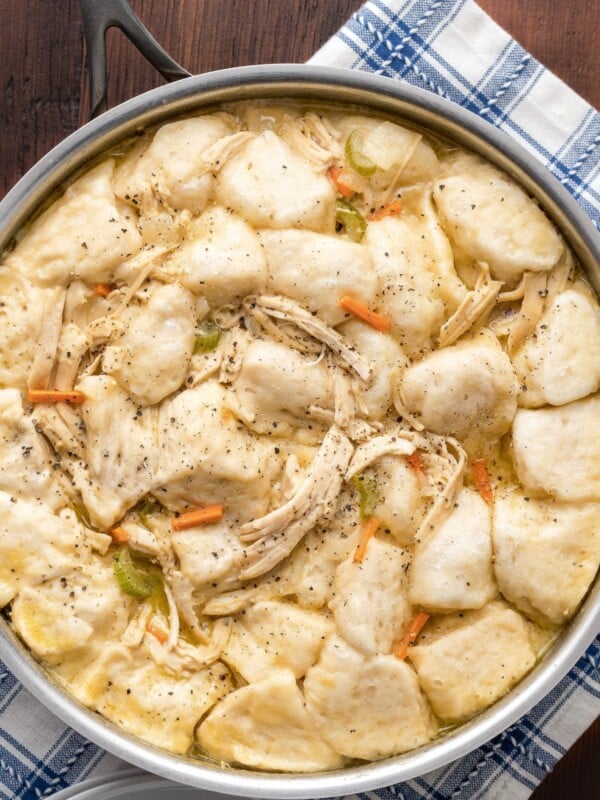 A pot filled with chicken and dumplings with fluffy biscuits and tender chicken in a creamy soup with carrots, onion and celery.