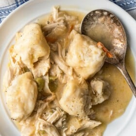 A serving of creamy chicken and dumplings with biscuits on a plate with a spoon.