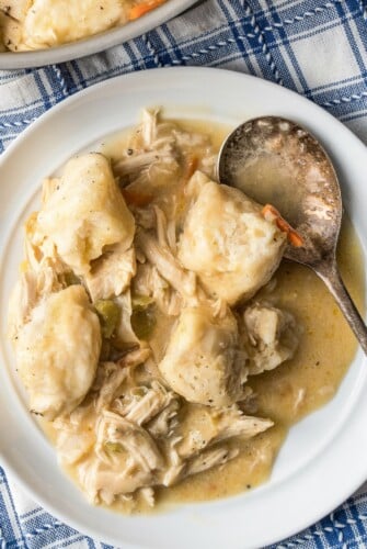 A serving of creamy chicken and dumplings with biscuits on a plate with a spoon.