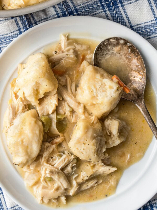 A serving of creamy chicken and dumplings with biscuits on a plate with a spoon.