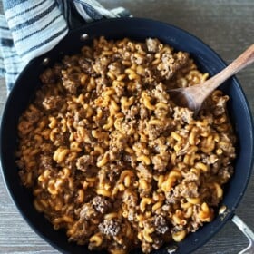 A skillet filled with homemade hamburger helper with a wooden spoon scooping out a serving.