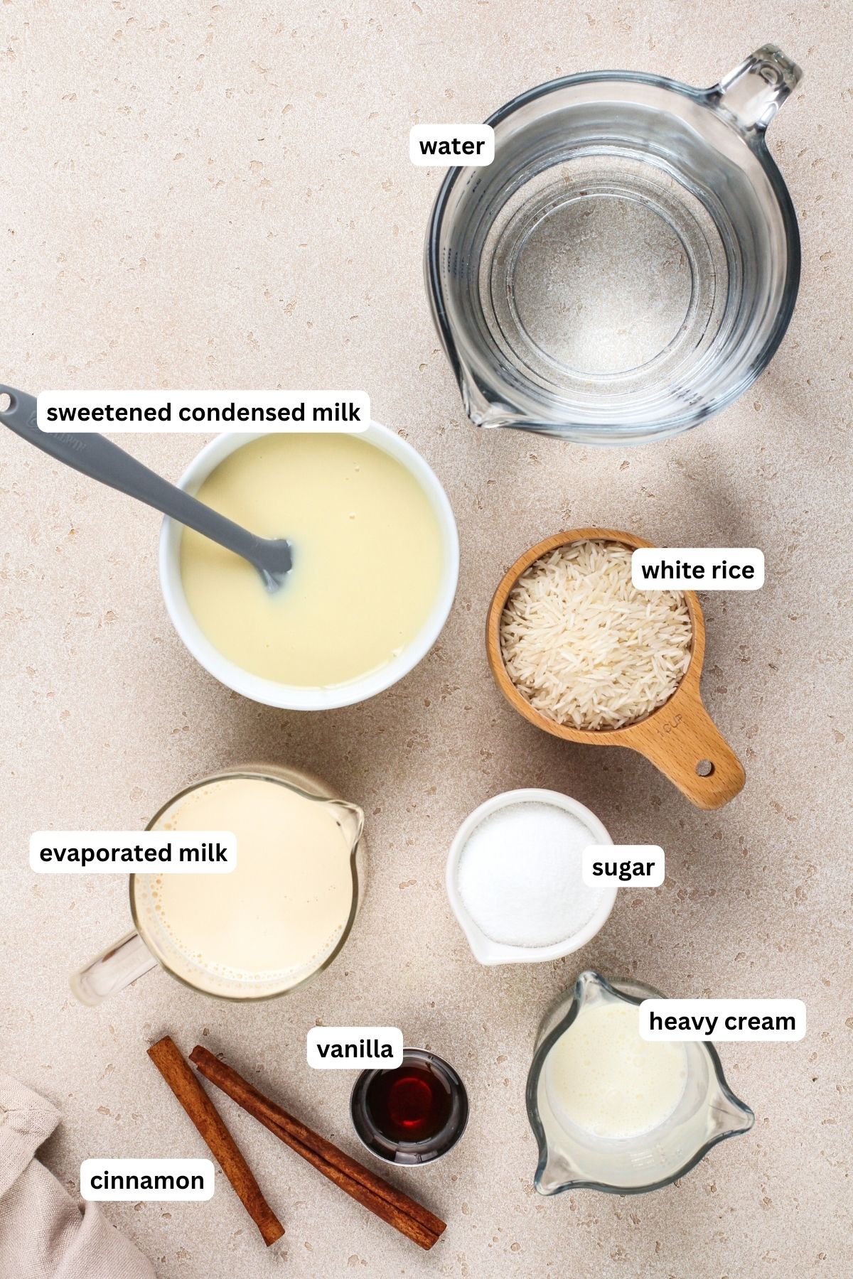 Ingredients for homemade horchata recipe arranged in bowls. From top to bottom: water, sweetened condensed milk, white rice, evaporated milk, granulated sugar, heavy cream, vanilla and cinnamon sticks.