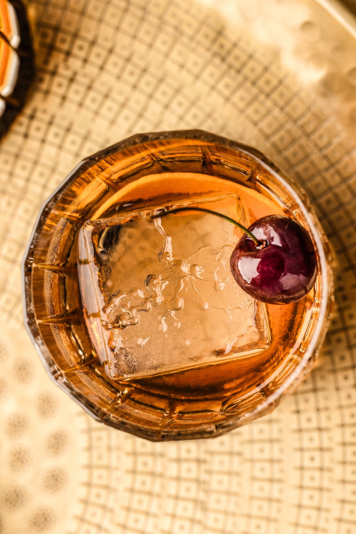 Old fashioned cocktail served in a short glass with a large cube ice cube, orange peel and cherry for garnish.