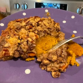 A serving of pumpkin dump cake with toffee and pecan topping on a plate with a fork cutting a bite.