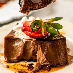 A fork scooping up a bite of rich and creamy chocolate flan.