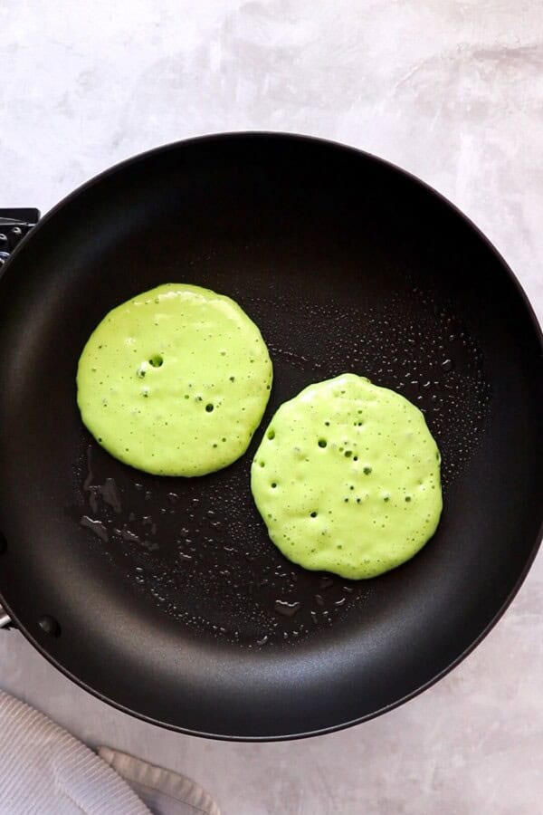 Two green grinch pancakes in a skillet being cooked.