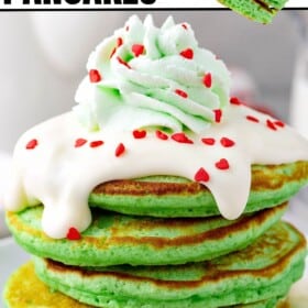 A plate of Grinch pancakes with cream cheese frosting, green whipped cream and red heart sprinkles on top.