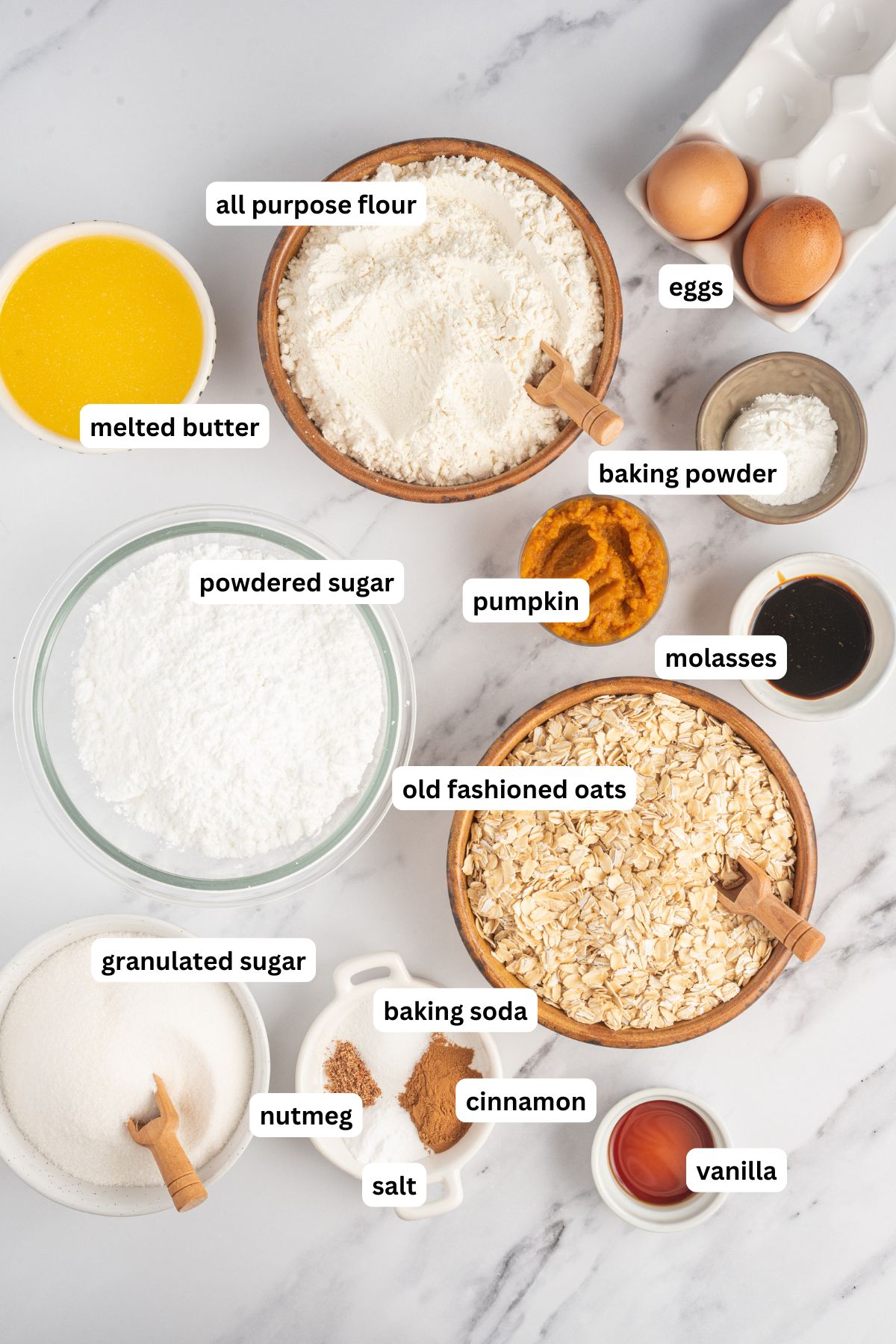 The ingredients for iced pumpkin oatmeal cookies recipe in order from top to bottom: melted butter, all purpose flour, eggs, baking powder, pumpkin, powdered sugar, molasses, old fashioned oats, granulated sugar, baking soda, nutmeg, cinnamon, salt, vanilla.