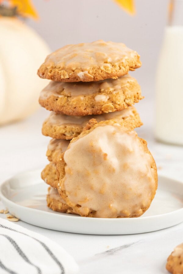 A stack of soft baked pumpkin oatmeal cookies with icing on a plate.