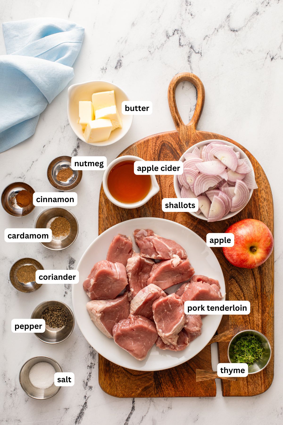 Ingredients for pork with apples recipe in order from top to bottom: butter, nutmeg, cinnamon, apple cider, shallots, cardamom, apple, coriander, pepper, salt, pork tenderloin, thyme.