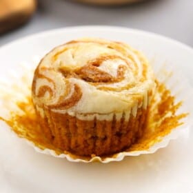 A pumpkin cream cheese muffin on a plate with the liner being pulled off.