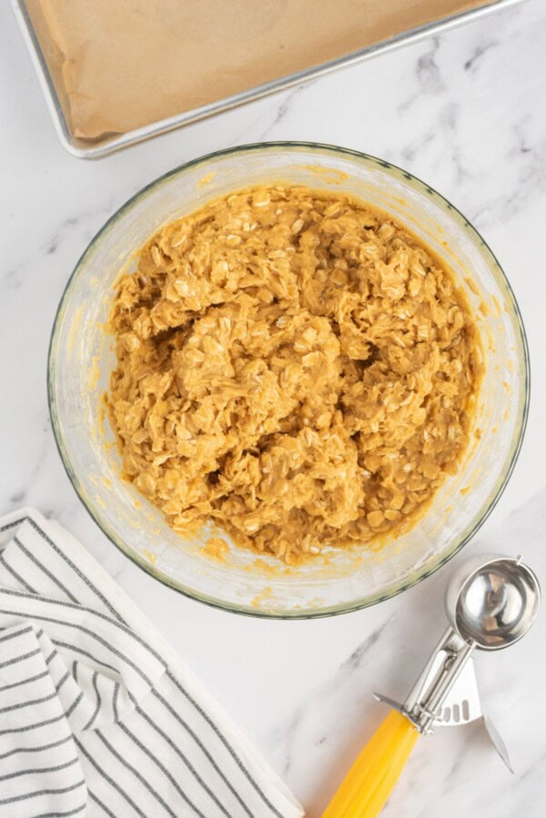 Oatmeal pumpkin cookie dough in a bowl with a cookie scoop on the side.