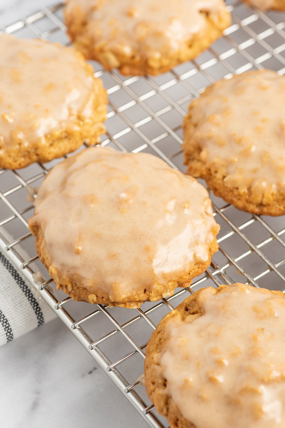 Several soft pumpkin oatmeal cookies with frosting are cooling on a wire rack.