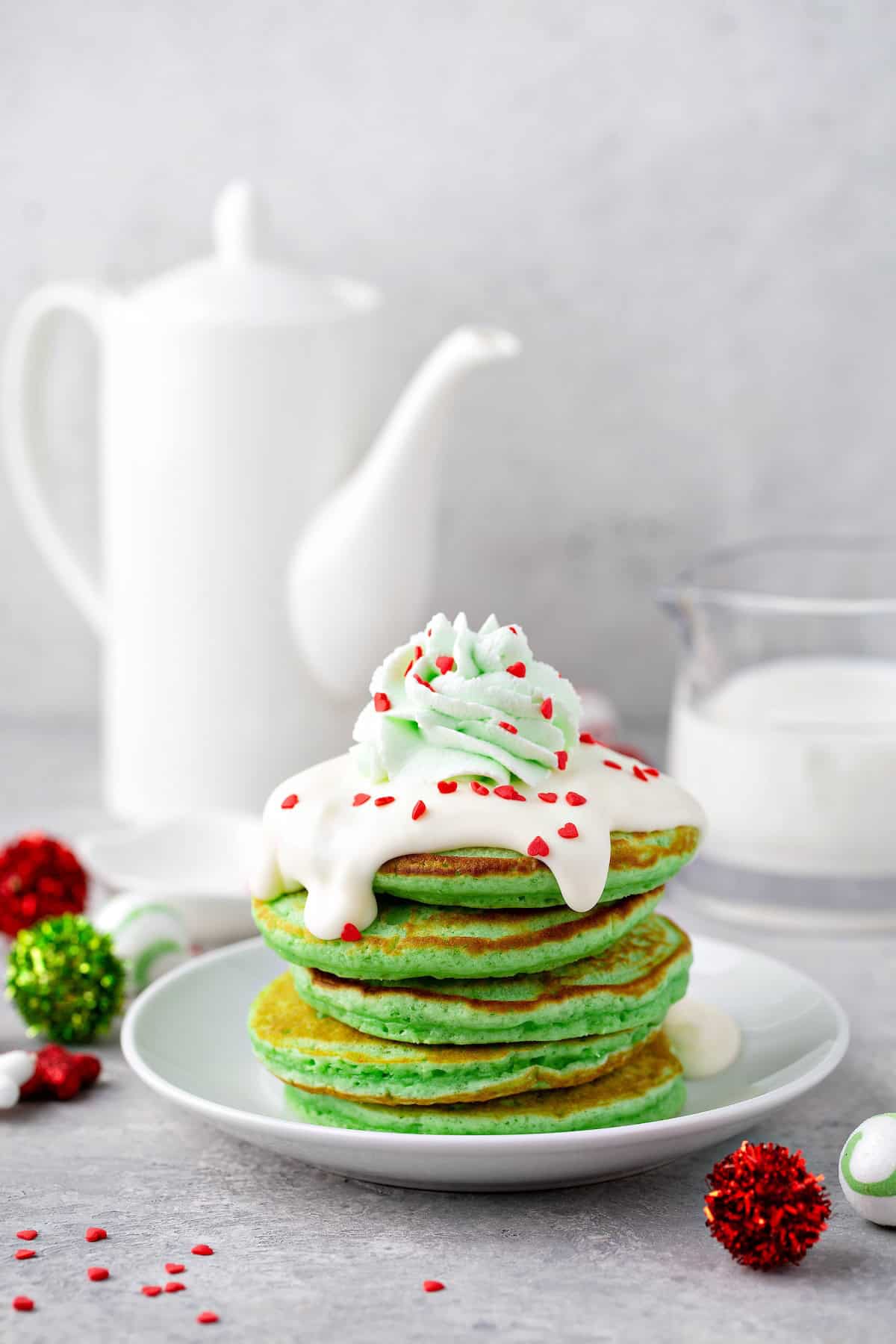 A stick of red and green Christmas pancakes with red heart sprinkles and cream cheese frosting on top.