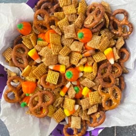 A halloween bowl filled with halloween Chex mix with candy corn and pretzels.