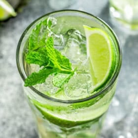 A glass filled with mint mojito cocktail with a lime wedge garnish.