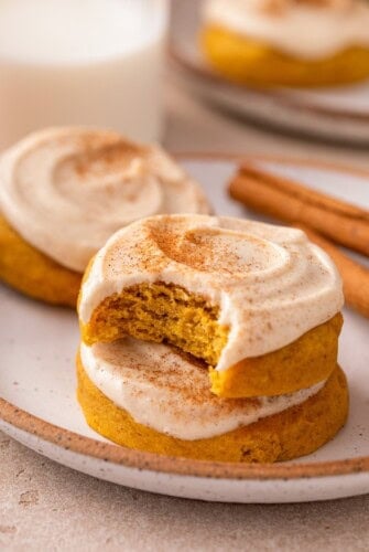 Easy frosted pumpkin cookies on a plate next to cinnamon sticks.