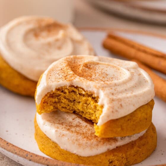 Easy frosted pumpkin cookies on a plate next to cinnamon sticks.