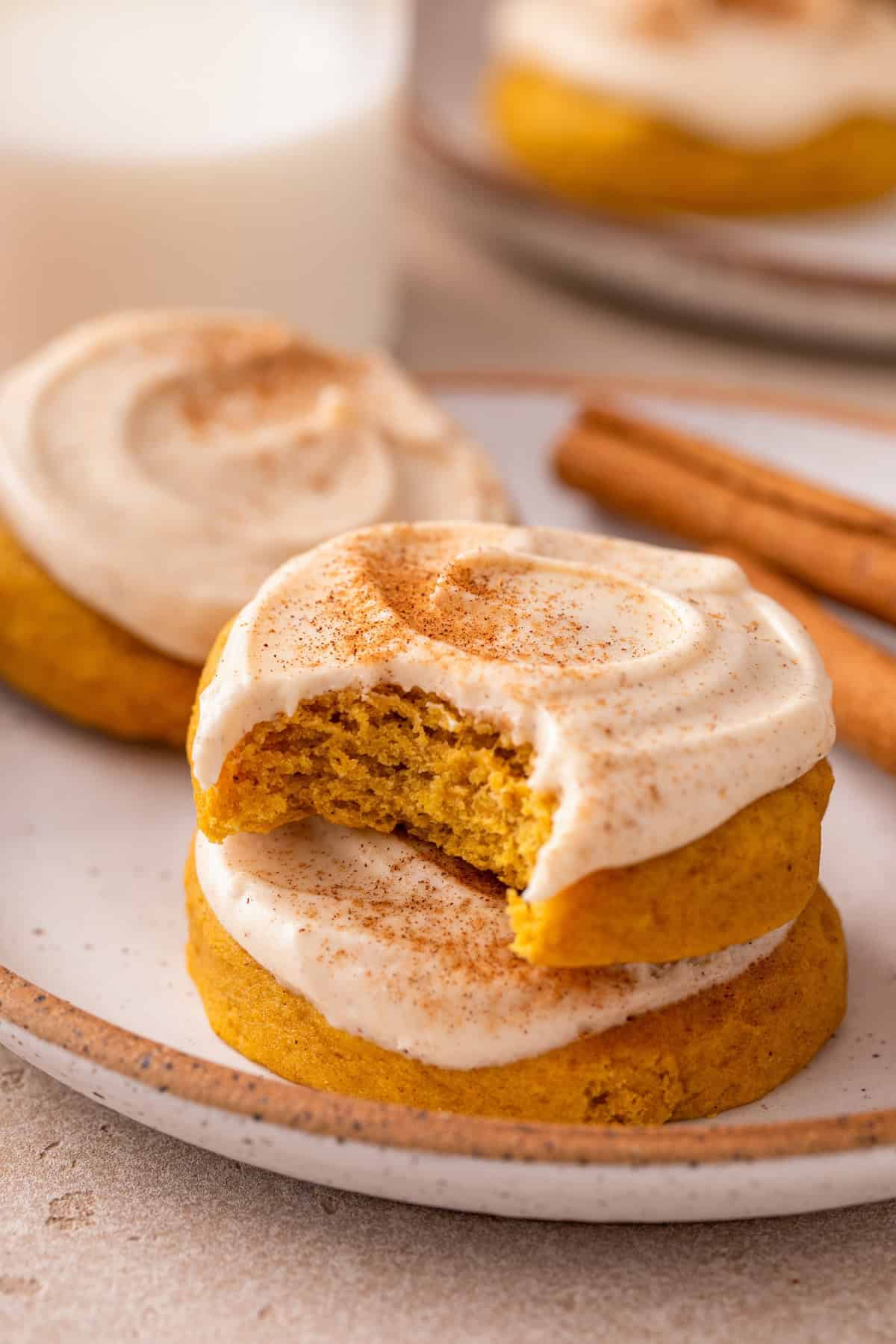 Easy frosted pumpkin cookies stacked on a plate with a bite taken out of the top cookie.