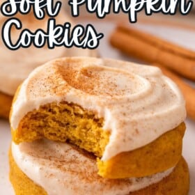 Two soft pumpkin cookies with cream cheese frosting stacked on top of each other with a bite taken out of the top cookie.